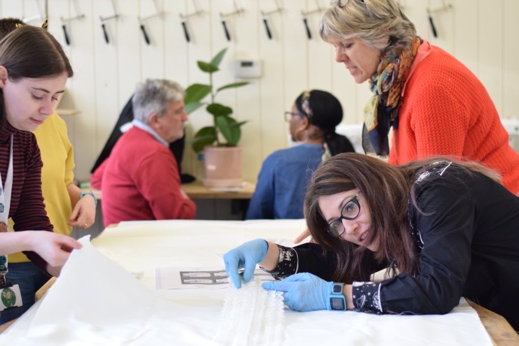 Three volunteers stand around a table working on a shroud