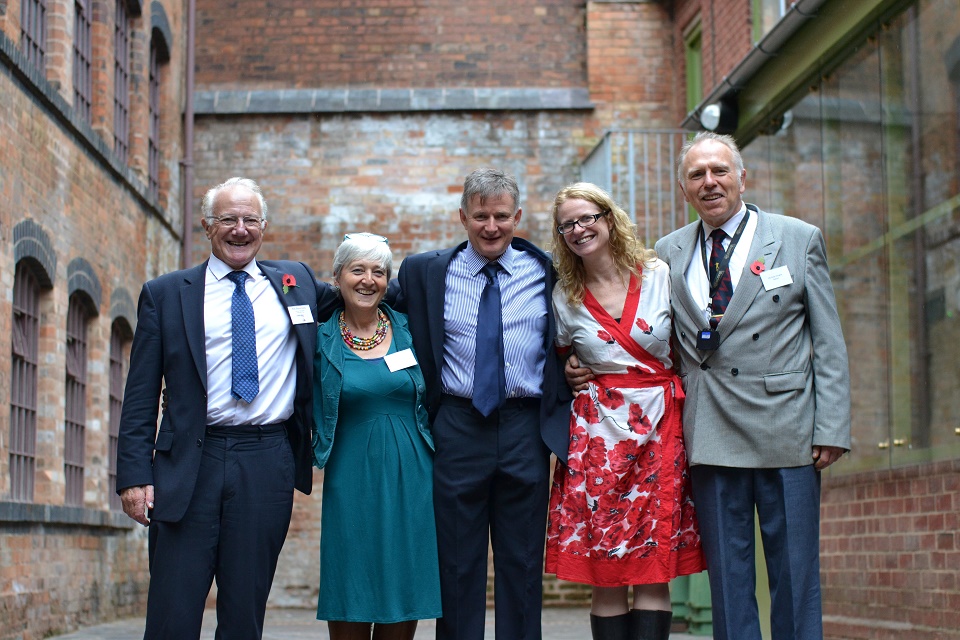 Group photo showing three men and two women standing in courtyard with arms around each others shoulders
